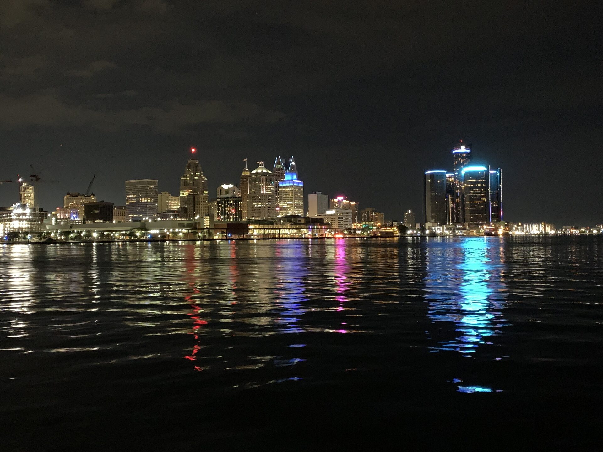 The Detroit skyline lit up at night, reflected on the water from Windsor